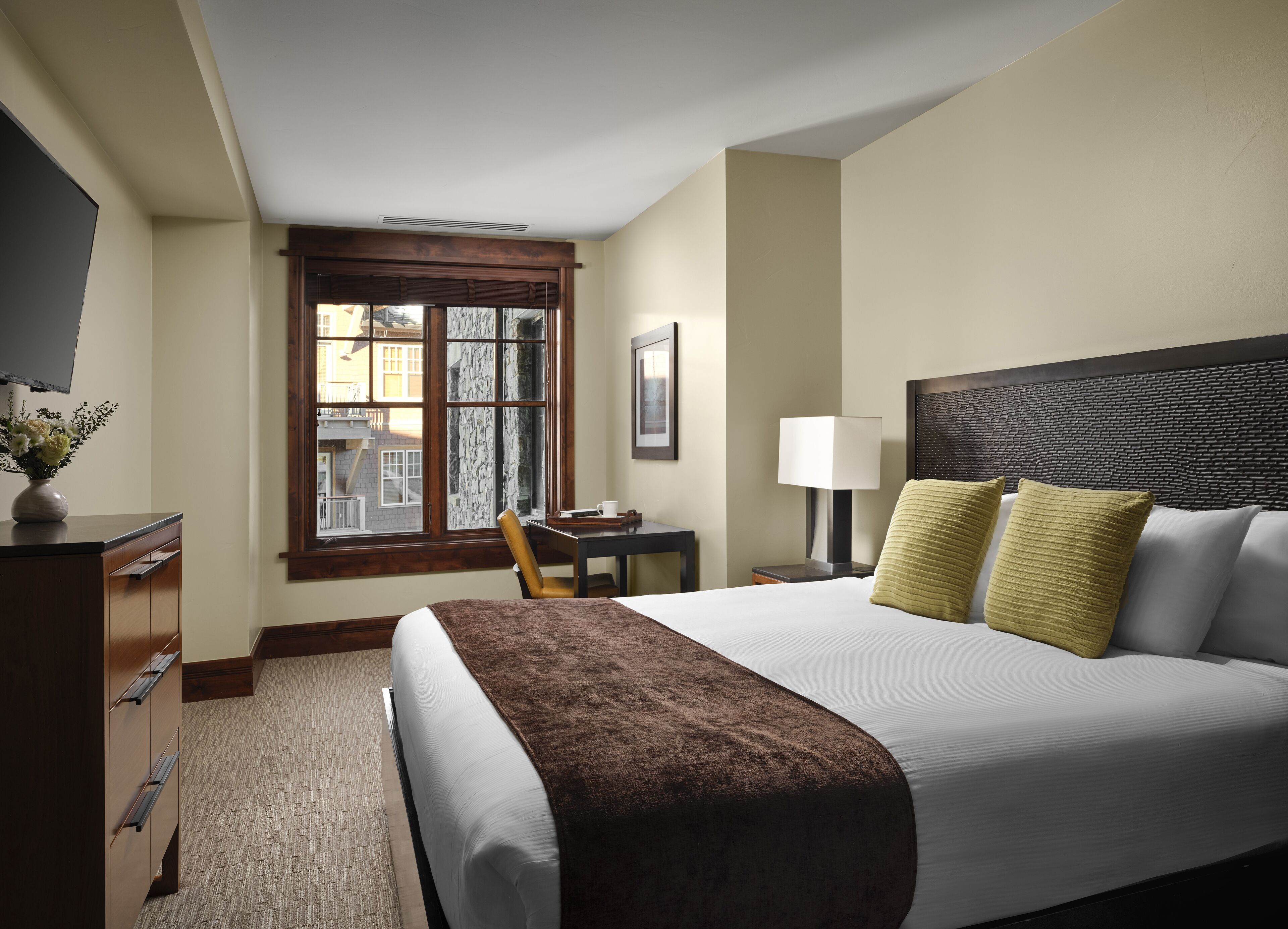 Une chambre d’hôtel avec un grand lit, un bureau, une chaise, une fenêtre donnant sur un beau paysage et un téléviseur situé à gauche.