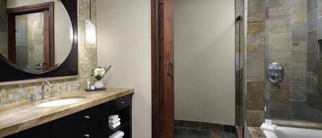 Un baño con un espejo grande, un lavabo, un tocador con cajones, una zona de ducha con puerta de cristal y suelo de baldosas.