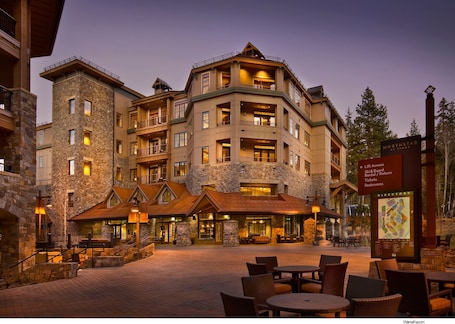 A multi-story hotel with stone and wood exterior, outdoor seating area, and a directory sign.
