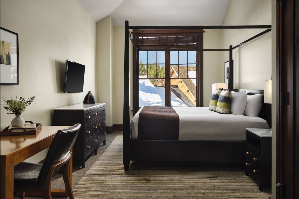 Une chambre à coucher avec un lit à baldaquin, un bureau avec une chaise, une commode et un téléviseur fixé au mur.