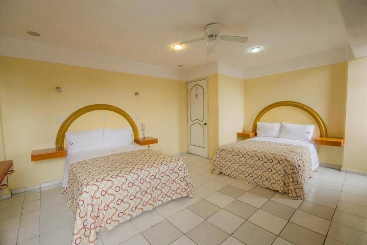 Habitación de hotel con dos camas, cada una con cabecera, mesita de noche y mesilla.