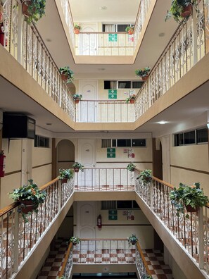 A multi-level atrium with a checkered floor, metal railings, and potted plants. - Hotel Central Puebla (Puebla)