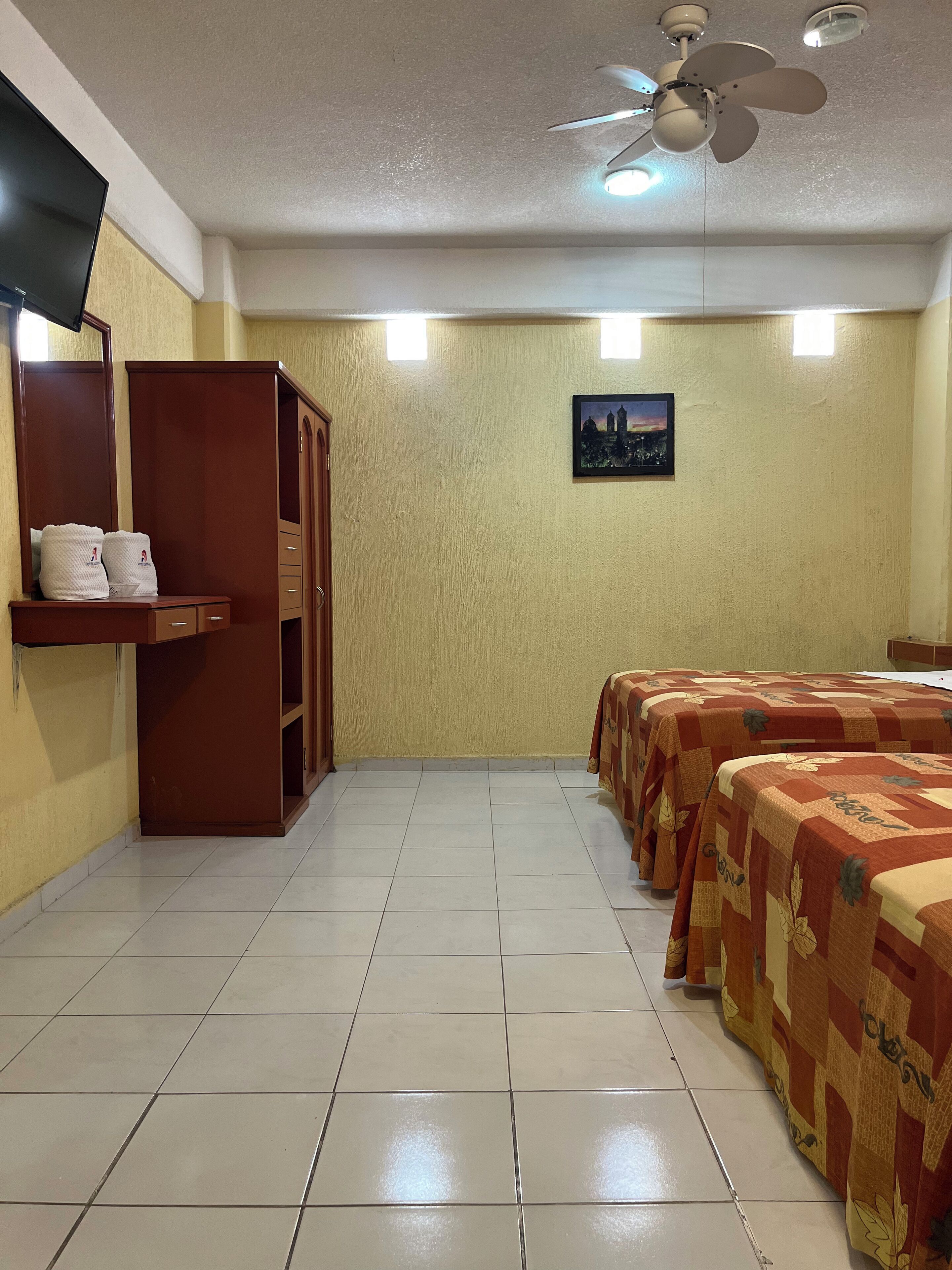 Una habitación de hotel con cama, armario, televisor de pantalla plana y ventilador de techo.