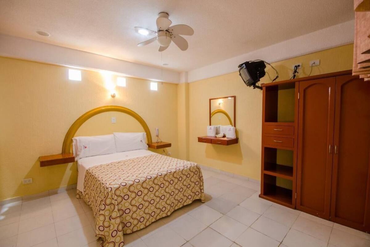 Habitación de hotel con cama, ventilador de techo, mesita de noche, espejo y armario.