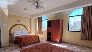 Habitación de hotel con una cama grande, una cama más pequeña, un armario, un ventilador de techo y una ventana con cortinas.