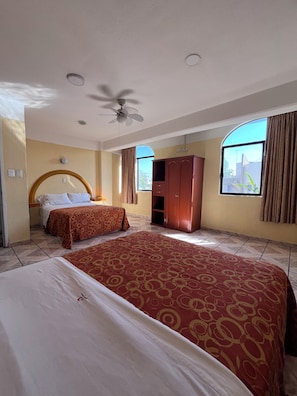 Habitación de hotel con una cama grande, una cama más pequeña, un armario, un ventilador de techo y una ventana con cortinas.