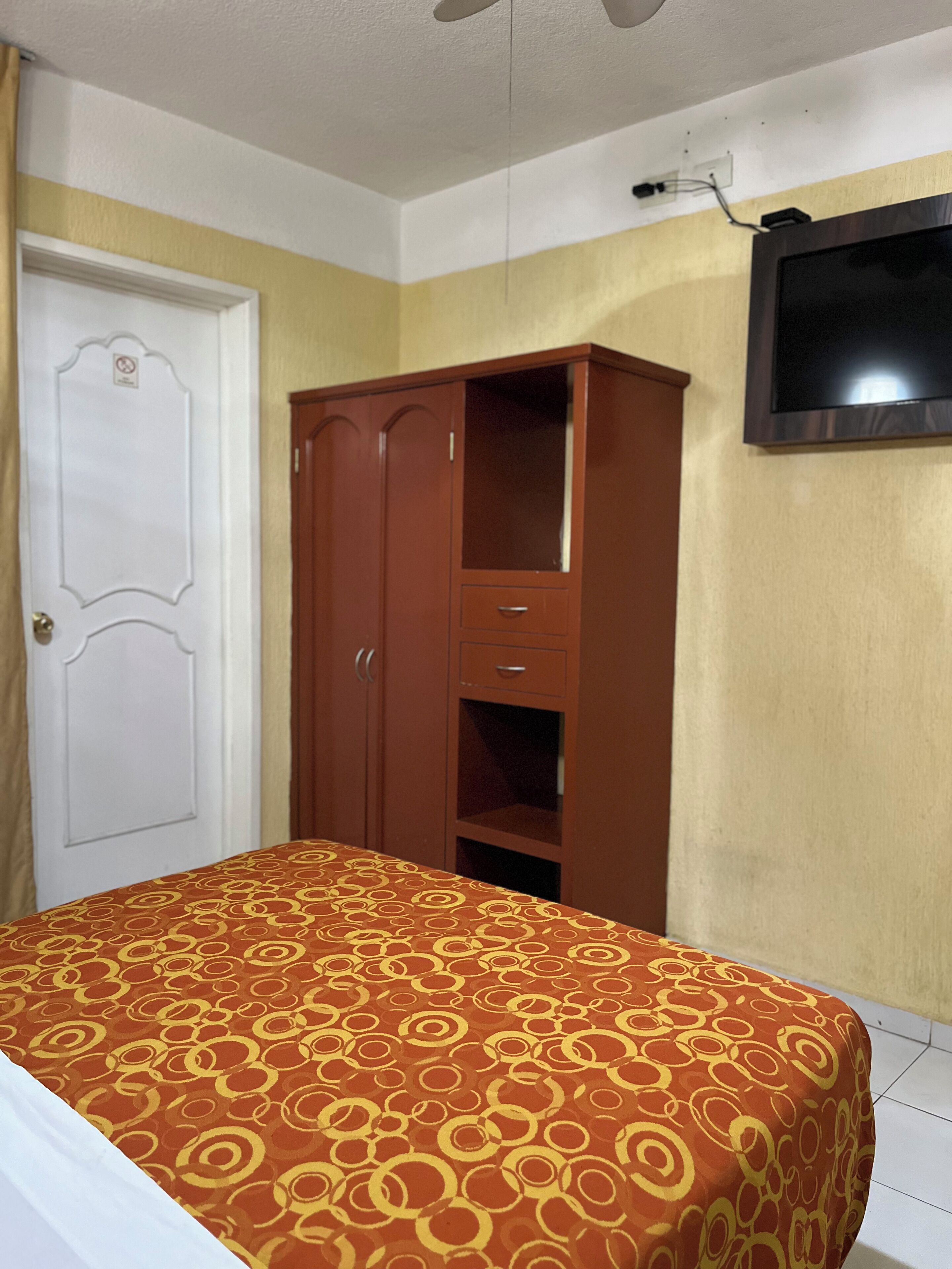 Un dormitorio con cama, armario y televisor montado en la pared.