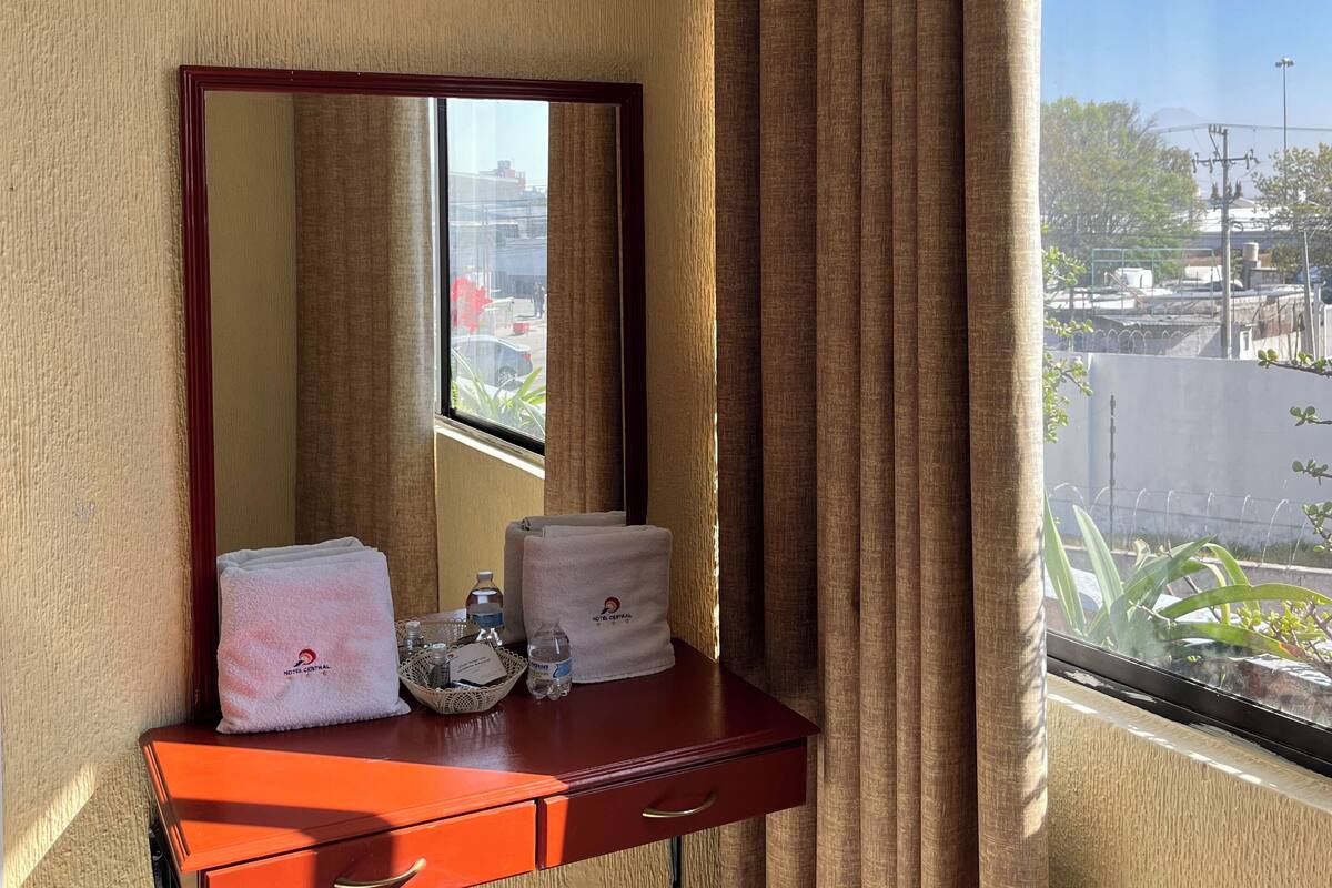 Habitación de hotel con tocador de madera, espejo y ventana con cortinas.