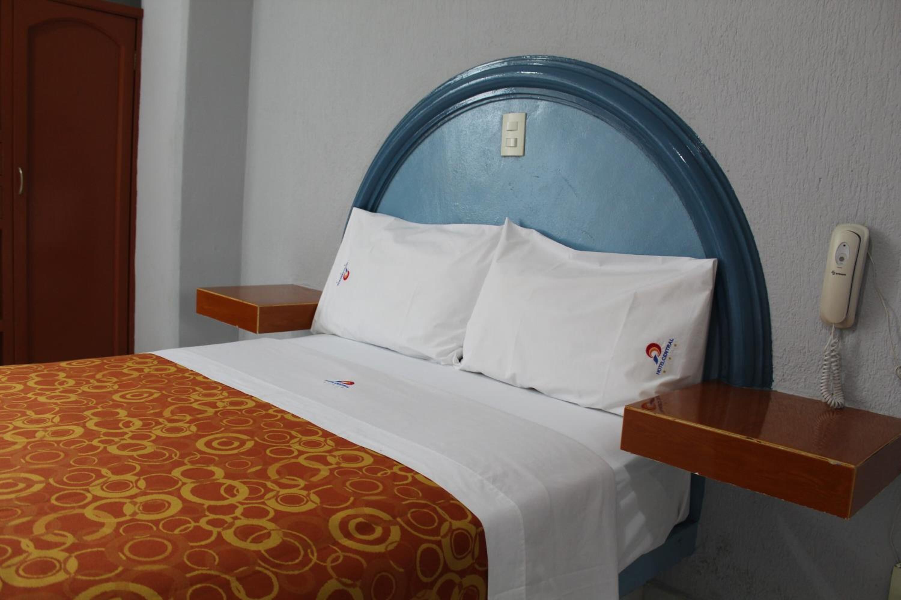 Una habitación de hotel con una cama, una mesita de noche de madera, un teléfono y un interruptor de luz en la pared.