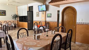 Un comedor con mesas y sillas, un televisor montado en la pared y una puerta con un cartel de 'SALE'.