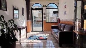 Un vestíbulo de hotel con suelo de baldosas, ventilador de techo, mostrador de recepción, sofá y planta en maceta.