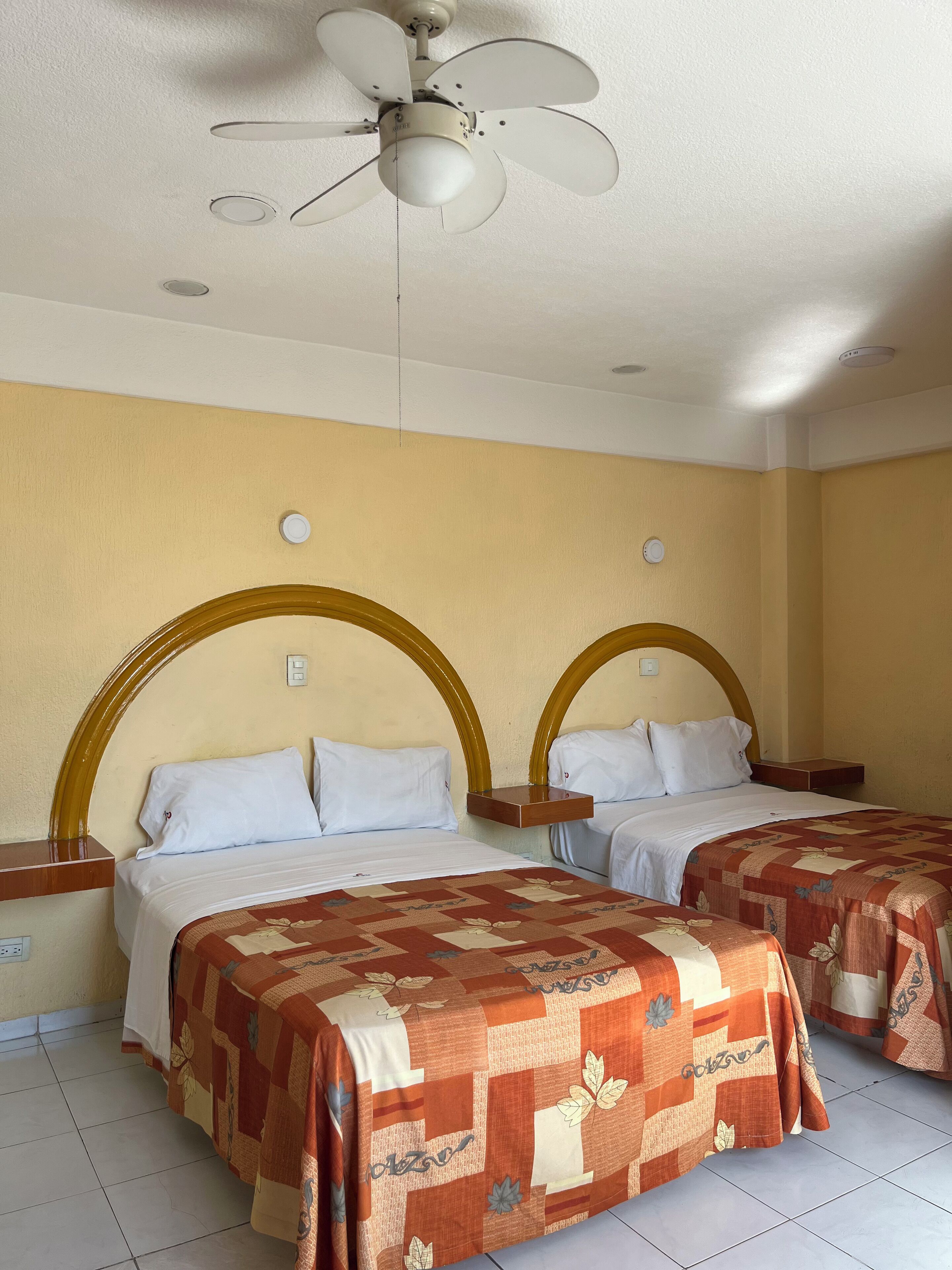 A hotel room with two beds, a ceiling fan, and a small table between the beds.
