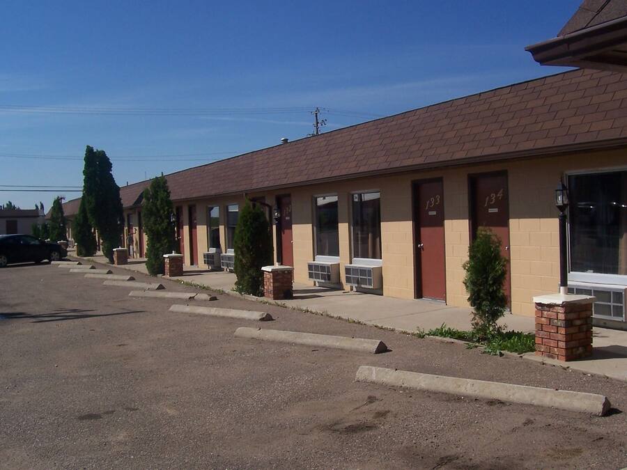 A row of motel rooms with individual doors, air conditioning units, and small brick planters.