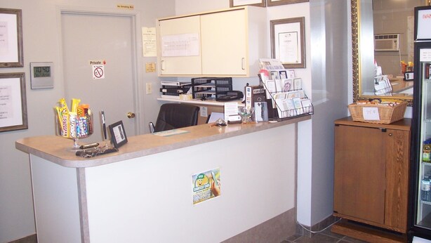 A reception desk with a counter, framed certificates, a private sign, a digital clock, and a refrigerator with a price tag. - Ivanhoe Motel (Lloydminster)