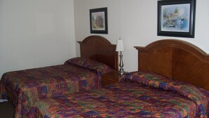 A hotel room with two beds, each with a patterned bedspread, a wooden headboard, a bedside table with a lamp, and two framed pictures on the wall. - Ivanhoe Motel (Lloydminster)