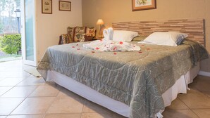A bedroom with a wooden ceiling, a bed with a floral bedspread, a bedside lamp, and a framed picture on the wall. - Villa Belle Chalés (Campos do Jordão)