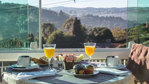 A table with breakfast items, two glasses of orange juice, and a scenic view through a window. - Villa Belle Chalés (Campos do Jordão)