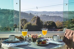 A table with breakfast items, two glasses of orange juice, and a scenic view through a window. - Villa Belle Chalés (Campos do Jordão)