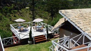 A rooftop deck with outdoor furniture and a pergola, surrounded by greenery and a building with a tiled roof. - Villa Belle Chalés (Campos do Jordão)