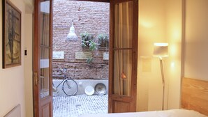 A hotel room with a bed, a wooden headboard, a lamp, and a view of a brick wall with plants and a bicycle outside. - Marcel de Buenos Aires (Buenos Aires)