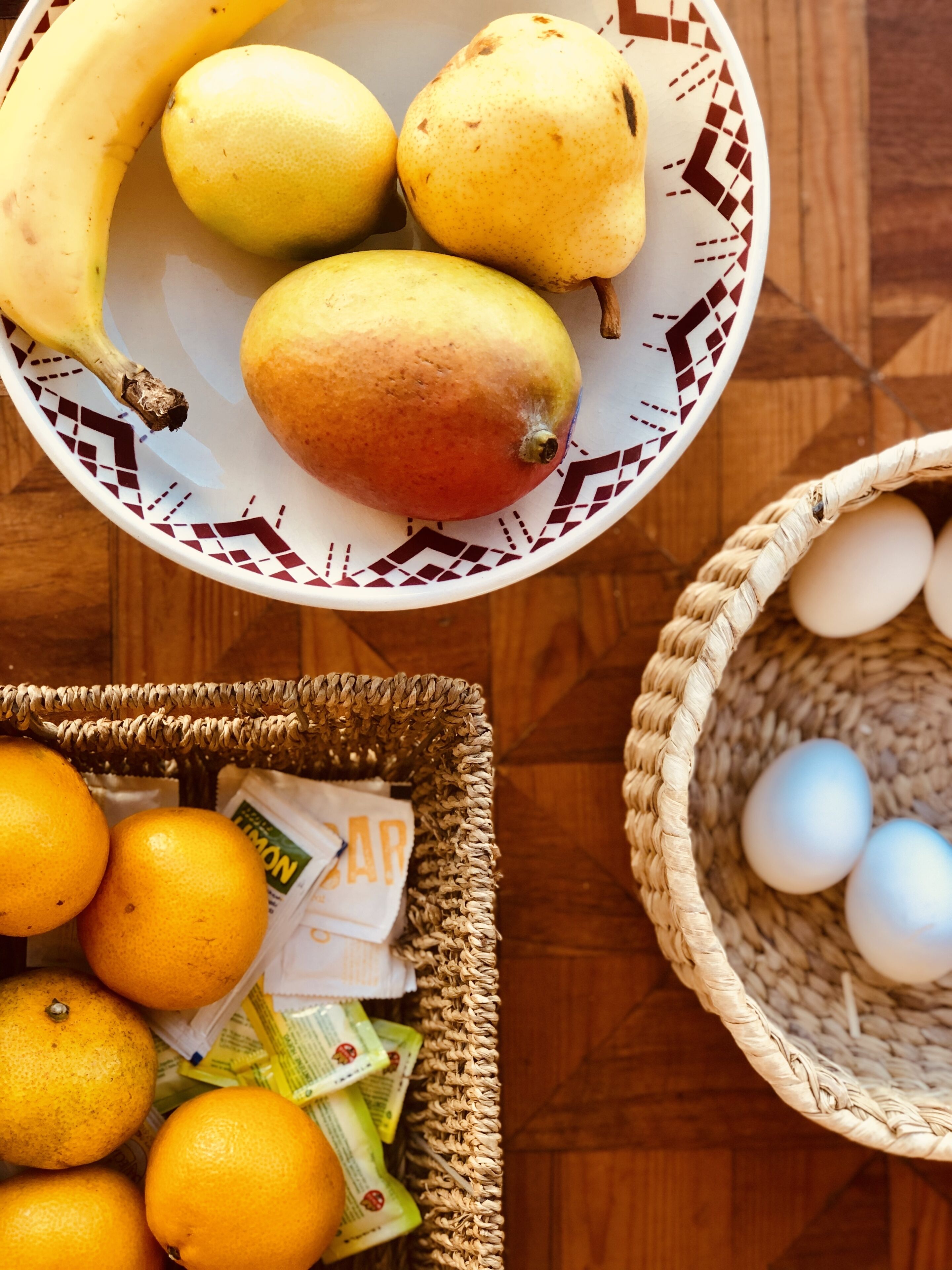A table with a plate of fruits, a basket of oranges, and a basket of eggs.
