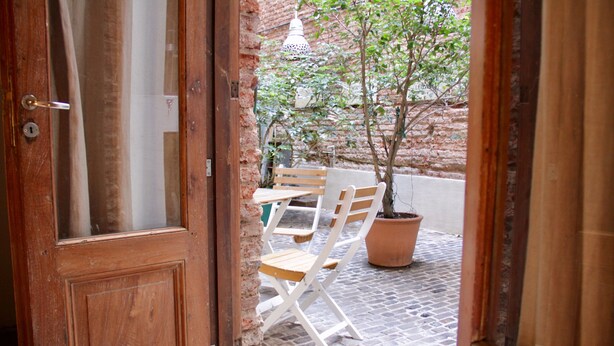 A wooden door with a glass panel, a brick wall, a potted plant, and a wooden bench outside. - Marcel de Buenos Aires (Buenos Aires)