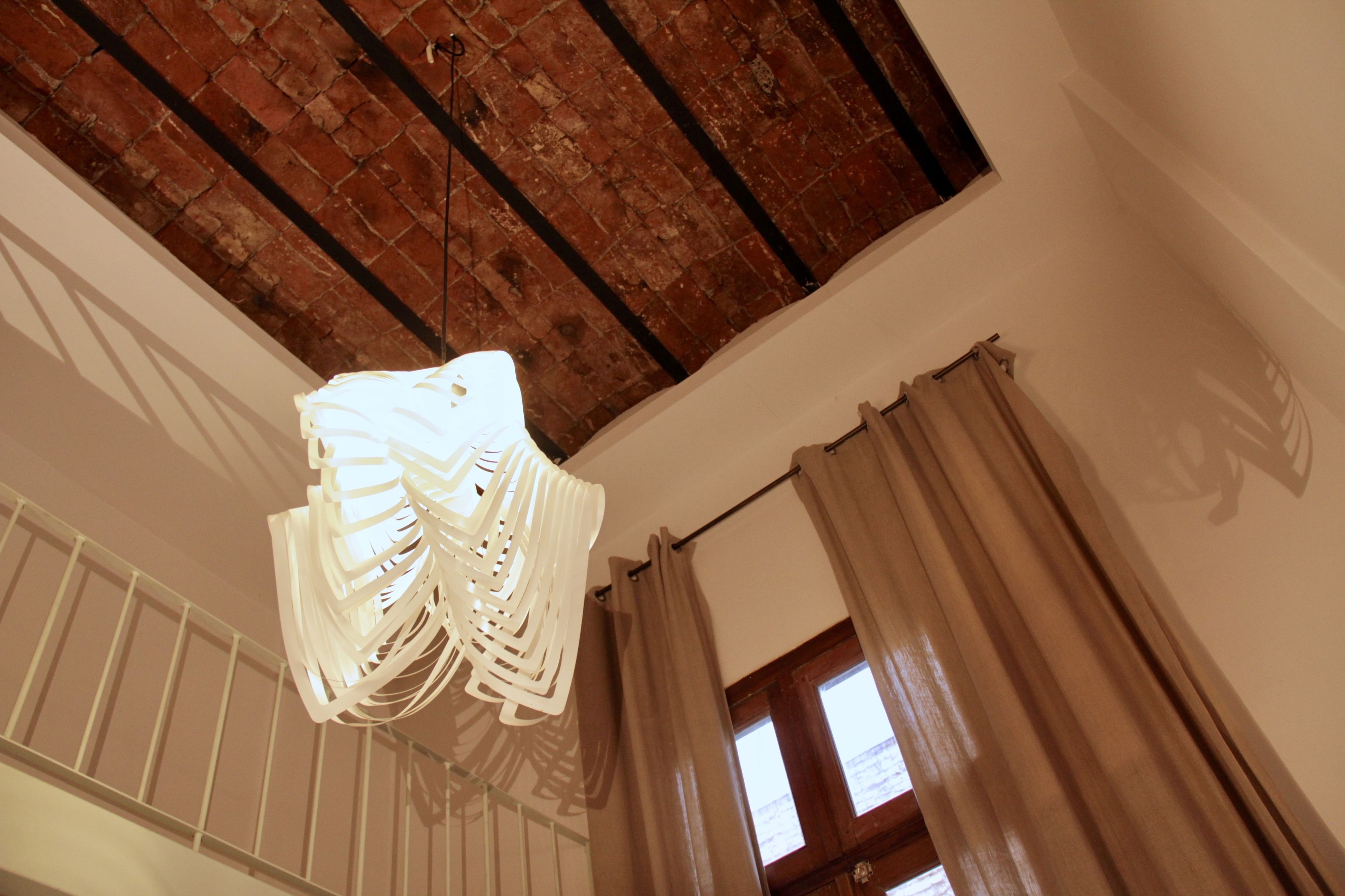 A room with a hanging light fixture, a window with curtains, and a brick ceiling.