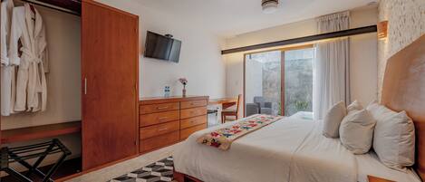 A bedroom with a large bed, a wooden wardrobe, a desk, and a television on the wall.