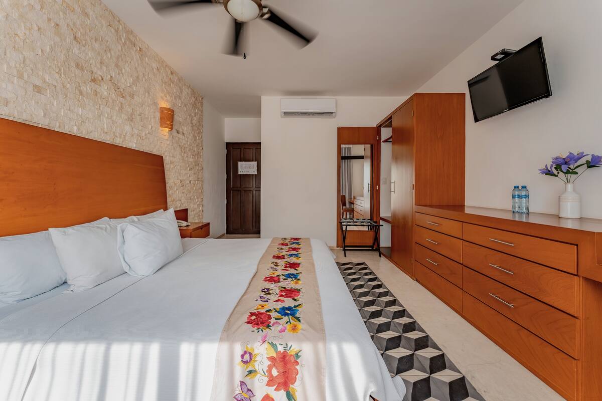 Une chambre d’hôtel comprenant un lit, une armoire en bois, un téléviseur à écran plat et un mur décoratif.