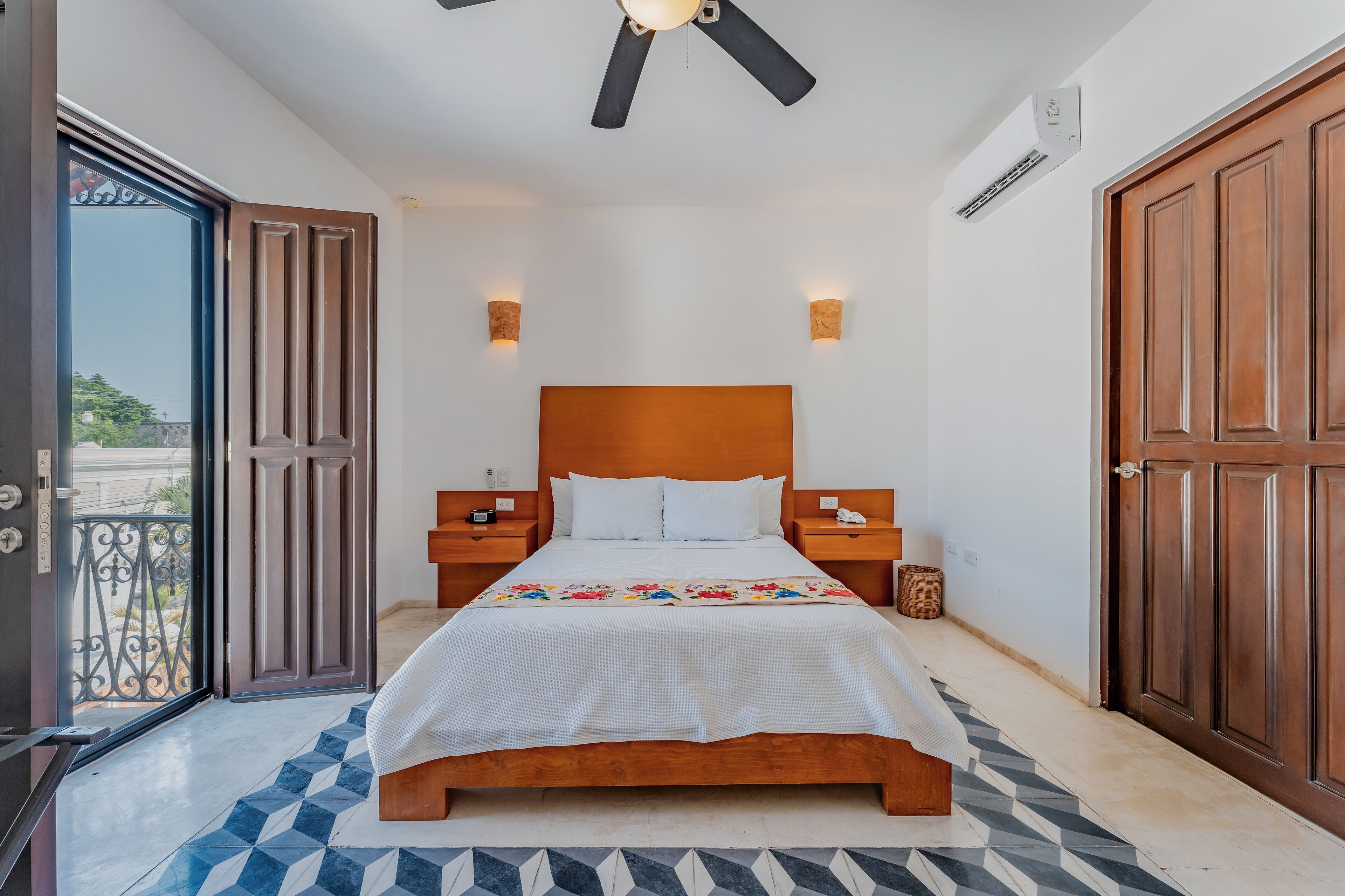 A bedroom with a wooden bed, two bedside tables, a ceiling fan, and a view through an open door.