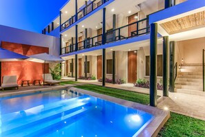 Un hotel moderno con piscina, mobiliario exterior y una zona de balcón bien iluminada.