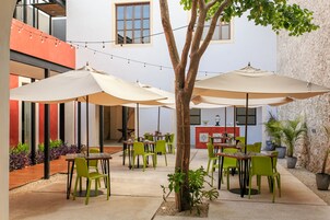Un patio al aire libre con mesas y sillas, luces colgantes y plantas en macetas.