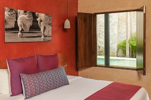 A bedroom with a bed, pillows, a painting, a window with a view, and a pendant light. - Casona 61 Boutique Hotel (Mérida)