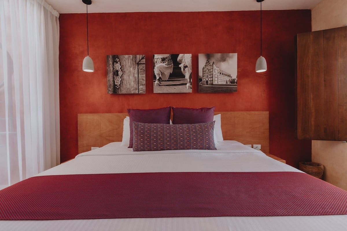 A hotel room with a large bed, red walls, and three framed pictures on the wall.