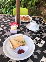 Una mesa con mantel estampado, un plato con dos tostadas y un tazón pequeño de mermelada, una taza de café, y un plato con panqueques y huevos.