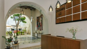 A reception area with a wooden reception desk, a glass wall, and a view of the outdoor seating area. - Casona 61 Boutique Hotel (Mérida)