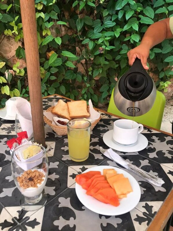 Una mesa servida con alimentos para el desayuno, incluyendo tostadas, un vaso de jugo, una taza de café, un plato de queso y un bol de yogur con granola.