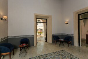 Eine Hotelhalle mit zwei blauen Sesseln, einem kleinen Tisch mit einem Buch und einem gemusterten Teppich.