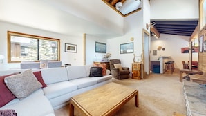 A living room with a sofa, armchair, wooden coffee table, and a dining area with chairs and a table. - Rainbow S 4 3 Bedroom Condo by RedAwning (Mammoth Lakes)