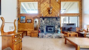 A cozy living room with a stone fireplace, wooden walls, and a mounted deer head. - Rainbow S 4 3 Bedroom Condo by RedAwning (Mammoth Lakes)