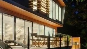 Una casa moderna con un amplio muro de cristal, un techo de listones de madera destacado y una terraza visible.