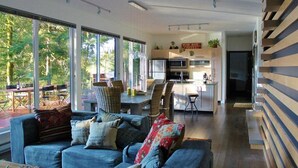 Una sala de estar moderna con sofá y sillones, un comedor con mesa y sillas, y una cocina con una isla central.