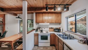 A compact kitchen with wooden cabinets, a stove, a sink, and a dining area with a wooden table.