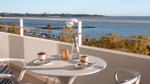 A balcony with a table set for two, overlooking a beach and the sea. - Dazzler by Wyndham Colonia (Colonia del Sacramento)