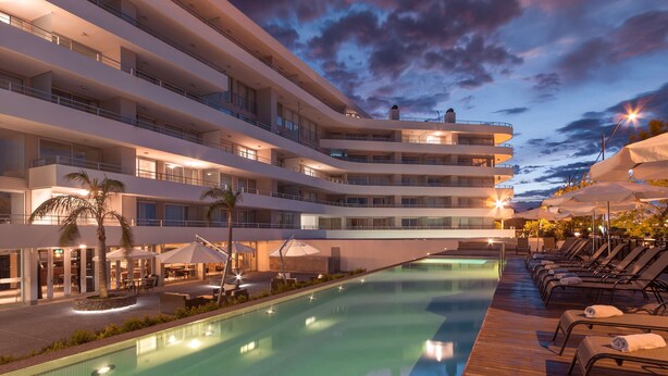 A multi-story hotel with a swimming pool, outdoor seating, and a sunset sky. - Dazzler by Wyndham Colonia (Colonia del Sacramento)
