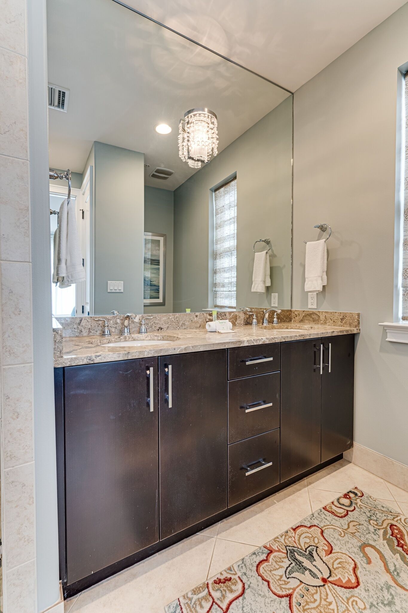 Un bagno moderno con mobili scuri, un grande specchio e un lampadario.