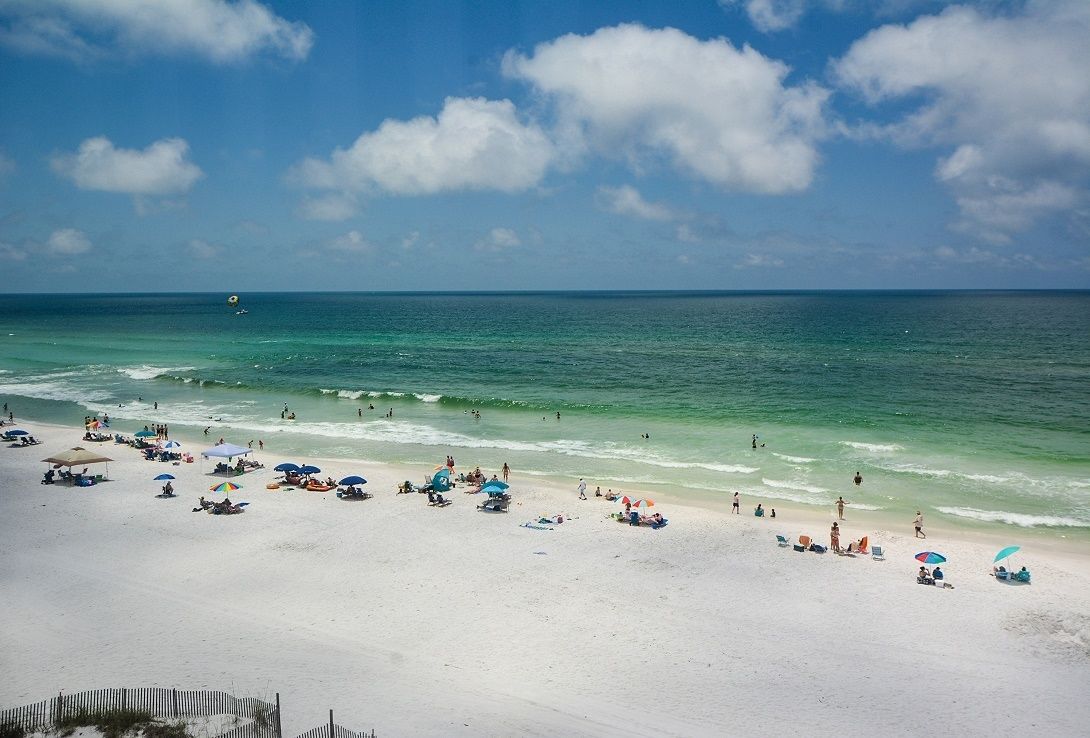 Een strand met helder turquoise water, wit zand en parasols.