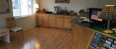 A kitchen with wooden cabinets, a coffee maker, a lamp, and a desk with a chair.