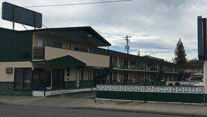 Un motel con fachada verde y beige, varias terrazas y un patio delantero cercado.