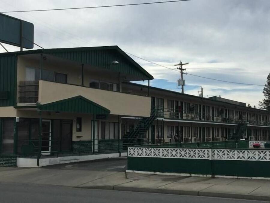 A motel with a green and beige exterior, multiple balconies, and a fenced front yard.